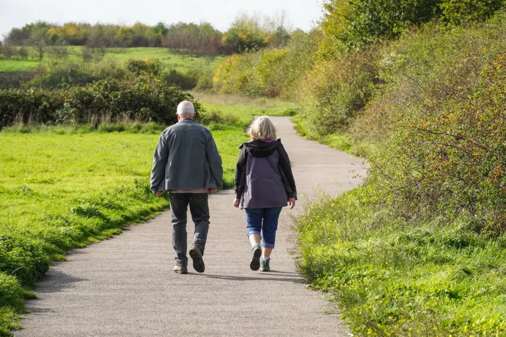 An older couple walking together along a country path, seen from behind