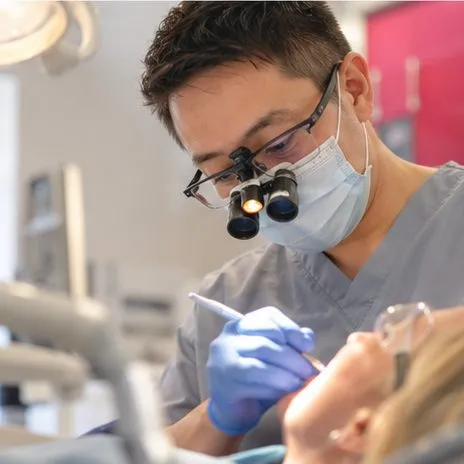 Dr Gavin Ho Fat wearing loupes and a mask, treating a patient