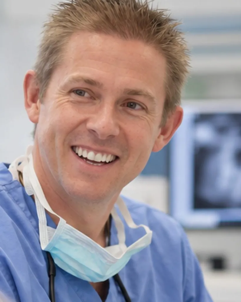 Dr Ross Cutts smiling during a consultation, with an X-ray on the screen behind him