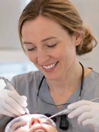 Hygienist smiling while cleaning a patient's teeth