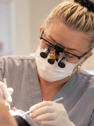 Hygienist with magnifying loupes treating a patient